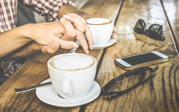 Close up of love couple drinking fresh cappuccino and having fun together - Youth relationship concept with young lovers together at coffee bar - Warm vintage retro filter with focus on crossing hands