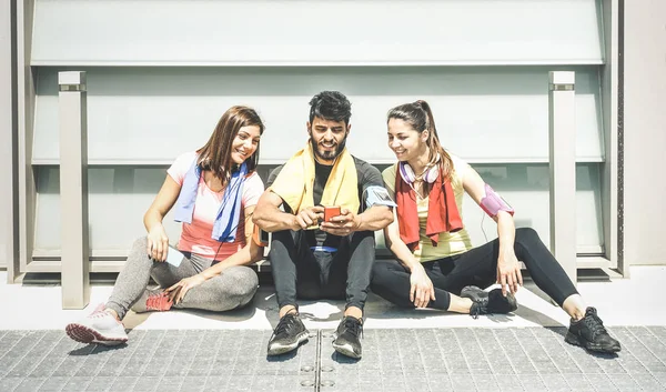 Happy friends having a break during sport fitness training using mobile smarphone - Young sporty people sharing moments with smartphone on social network - Technology concept on desaturated filter — стоковое фото