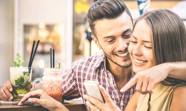 Giovane coppia di moda di amanti che giocano con lo smartphone cellulare al cocktail bar - Concetto di amore di relazione con fidanzato felice e fidanzata insieme dopo aver bevuto divertimento al primo appuntamento - Filtro vintage — Foto Stock