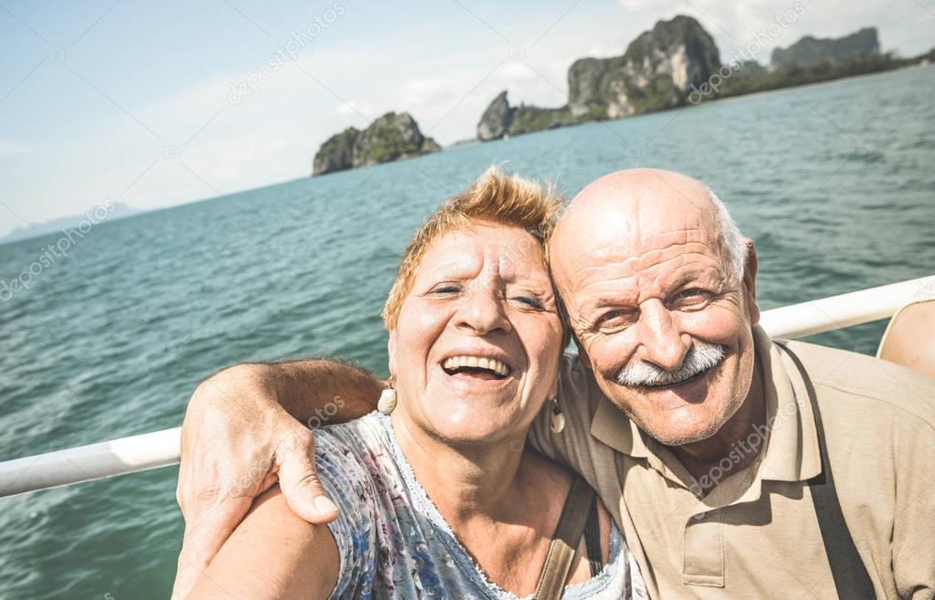 Happy retired senior couple taking travel selfie around world - Active elderly concept with people having fun together at Phang Nga bay Thailand - Mature people fun lifestyle - Retro contrast filter