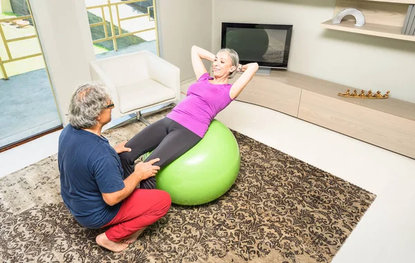 活跃的老年夫妇与瑞士球在家里-退休的人在健身房客厅里锻炼健身活动-培训辅导上紧缩坐 ups 腹部运动执行的夫人女人的成熟男人 — 图库照片