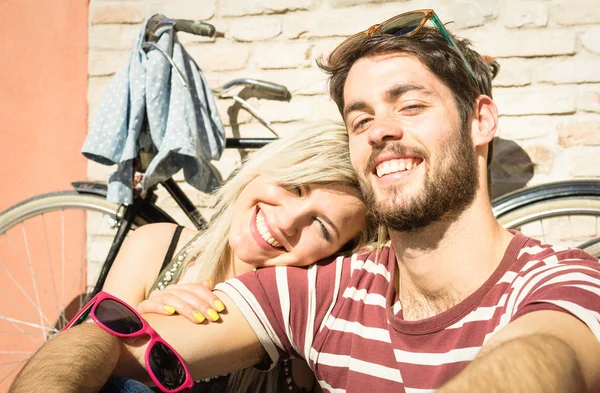 Happy hipster couple taking selfie at old town trip with vintage bicycle - Fun concept with alternative fashion city travelers - Handsome boyfriend with caucasian girlfriend - Warm bright vivid filter — Stock Photo, Image