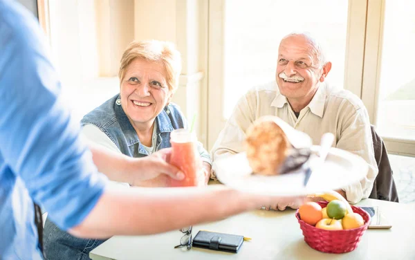 Camarero sirviendo a pareja de personas mayores comiendo en restaurante vegano - Hombre y mujer jubilados en ancianos activos divirtiéndose - Concepto de jubilación feliz con personas maduras juntas - Filtro brillante con enfoque en la señora —  Fotos de Stock