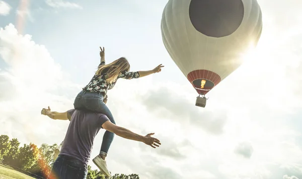 Happy couple in love on honeymoon vacation cheering at hot air balloon - Summer travel concept with young people travelers having fun at trip excursion - Vintage contrast retro filter with backlight — Stock Photo, Image