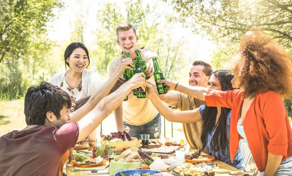 Junge multiethnische Freunde stoßen auf Grillparty an - Freundschaftskonzept mit fröhlichen Menschen, die Spaß im Hinterhof-BBQ-Sommerlager haben - Essen und Trinken schickes Picknick-Mittagessen - Fokus auf Bierflaschen — Stockfoto