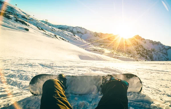 Snowboarder κάθεται στο ηλιοβασίλεμα στο να χαλαρώσουν τη στιγμή γαλλικές Άλπεις χιονοδρομικό θέρετρο - έννοια άθλημα χειμώνα με άντρα περιπέτεια στην κορυφή του βουνού που είναι έτοιμοι να βόλτα κάτω - πόδια άποψη με κιρκιριών και πορτοκαλί φίλτρο — Φωτογραφία Αρχείου