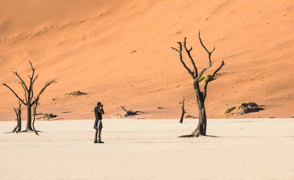 孤独的冒险旅行摄影师在 Deadvlei 火山口在索苏斯维雷疆土-纳米比亚世界著名沙漠-流浪概念与非洲自然奇观与独特的狂放的风景在纳米比亚 — 图库照片