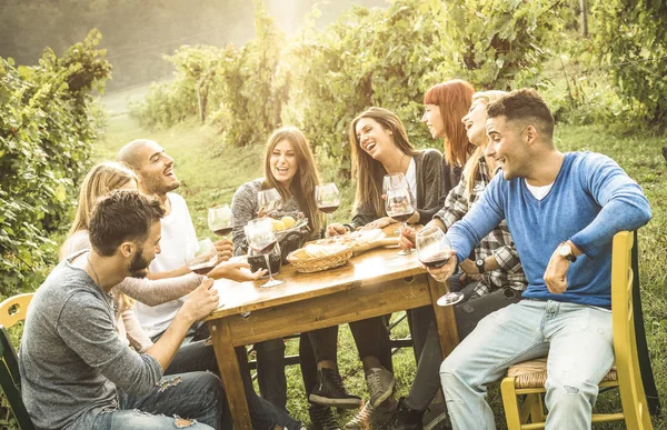 Amigos felizes se divertindo ao ar livre bebendo vinho tinto - Jovens comendo alimentos na época da colheita na vinícola da fazenda - Conceito de amizade juvenil com profundidade rasa de campo - Filtro de contraste quente — Fotografia de Stock