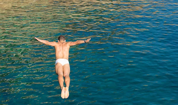 Cliff diver guy jumping in the blue sea from high rocks wall - Joyful freedom concept and carefree sensation feeling the pure connection with the nature - Natural vivid afternoon color tones — Stock Photo, Image