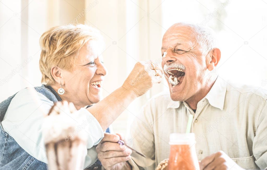 Happy retired senior couple in love enjoying bio icecream cup - Joyful elderly lifestyle concept - Wife feeding husband and having fun at bar cafe restaurant during evergreen vacation - Retro filter