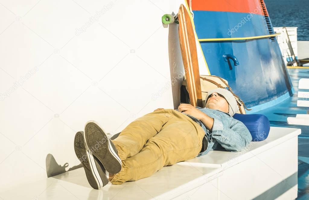 Young hipster man having rest on ferry boat passage holding smartphone  - Modern concept of inspired freedom and wander lifestyle - Cheap travel backpacking around the world - Warm afternoon filter