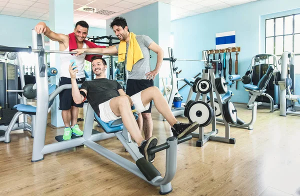 Group of sportive friends using mobile phone at gym fitness club - Happy sporty people in weight room training - Social gathering concept in sport lifestyle context - Main focus on guys interaction — Stock Photo, Image