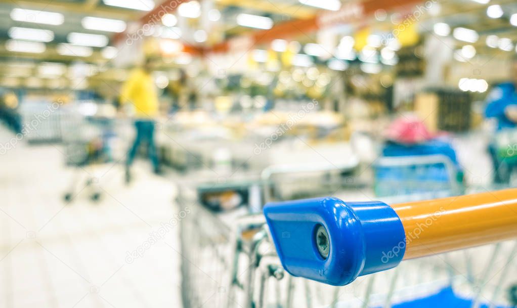 Blurred defocused bokeh of grocery supermarket - Consumerism concept in economic crisis moment at commercial center - Shallow depth of field with focus on shopping cart edge - Teal and orange filter