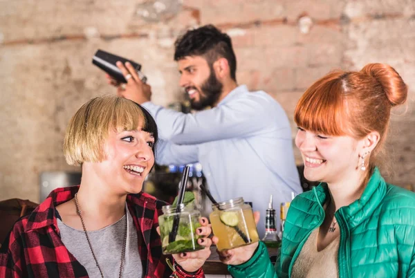 Et par kjærester som har det gøy på motecocktailbar Profesjonell barmann som rister alkohol bak unge fulle kvinner Nattklubbkonsept med kvinnelige kjærester som snakker sammen – stockfoto