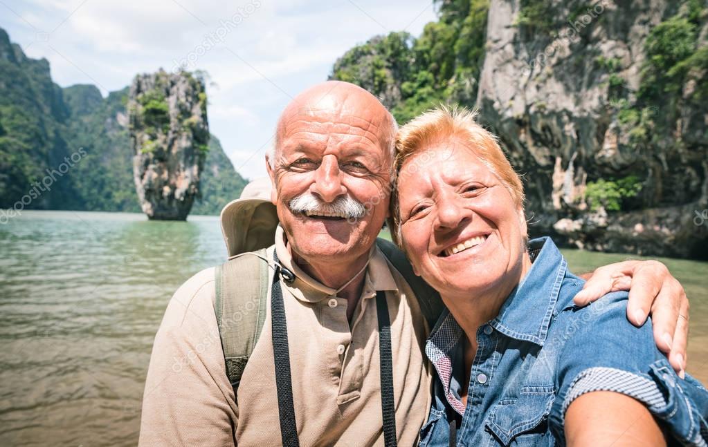 Happy retired senior couple taking travel selfie around world - Active elderly concept with people having fun together at James Bond Island in Thailand - Mature people lifestyle - Warm day filter
