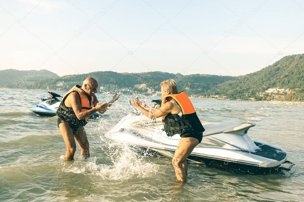 Senior happy couple having playful fun at jet ski on beach island hopping tour - Active elderly travel concept around the world with retired people riding water scooter jetski - Bright vintage filter