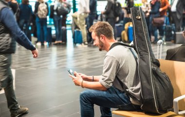 Hipster adam adam ve gitar sırt çantası - yüz odaklanmak ile mobil akıllı telefon - terminal kapısında bekleyen uçak için avare kişi - Yolculuk tutkusu seyahat gezi kavramı kullanarak Uluslararası Havaalanı'nda