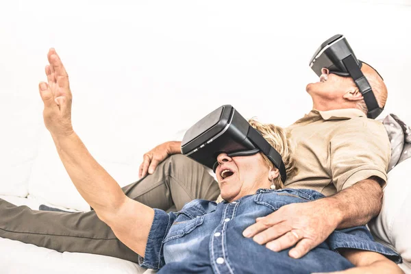 Pasangan dewasa senior bersenang-senang bersama dengan virtual reality headset duduk di sofa Happy pensiunan orang menggunakan modern vr kacamata tren baru dan teknologi konsep dan lucu aktif lansia — Stok Foto