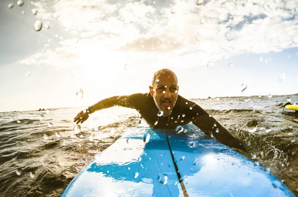 Surfer guy paddling with surfboard at sunset in Tenerife with unrecognizable people at surf boards on background - Sport travel concept with shallow depth of field with drops on lens as composition — Stock Photo, Image