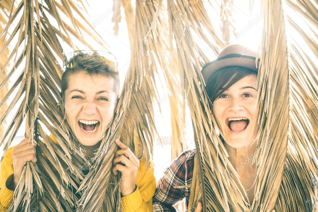 Happy playful girlfriends in love sharing time together at travel trip playing with palm tree - Women friendship concept with girls couple having fun on pure carefree mood - Bright sunset filter