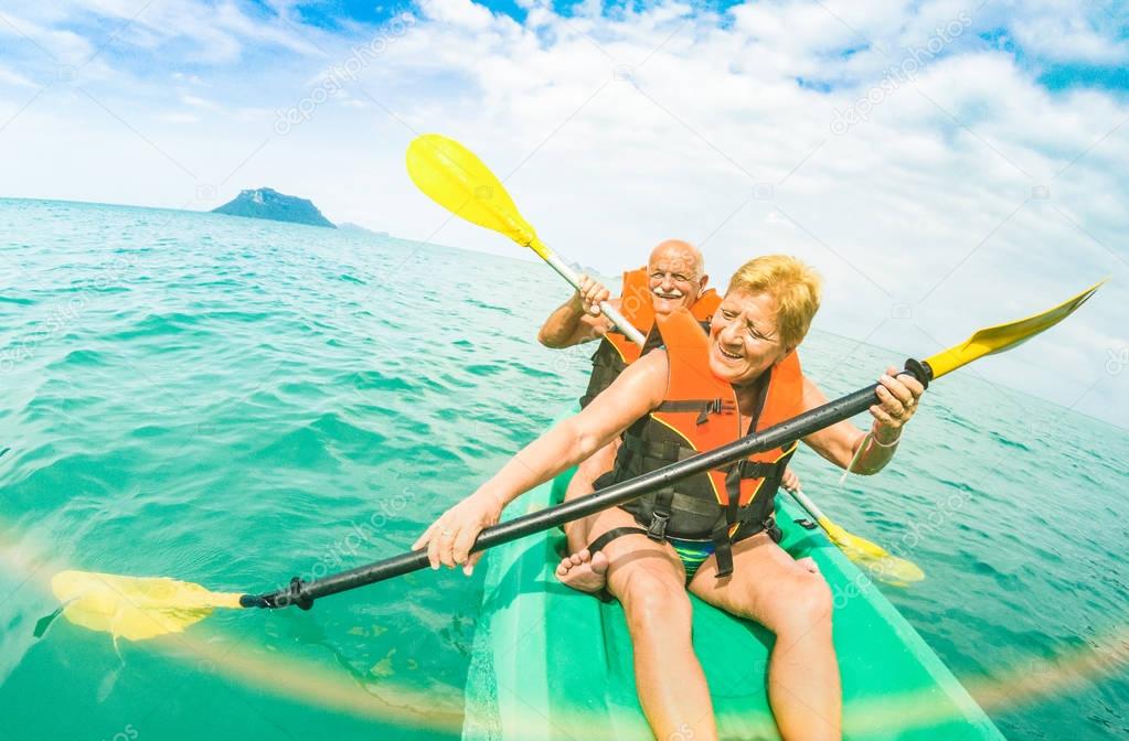 Senior happy couple taking travel selfie on kayak at Ang Thong marine park in Ko Samui - Trip to Thailand wonders - Active elderly concept around world - Tilted composition and sunshine flare filter
