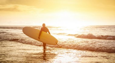 Adam sörfçü Tenerife - Surf uzun tahta eğitim Uygulayıcı eylem - spor seyahat konsepti ile sof odak su kenarında ayak - sıcak güneş renk foltered tonlarda günbatımında sörf ile yürüyüş