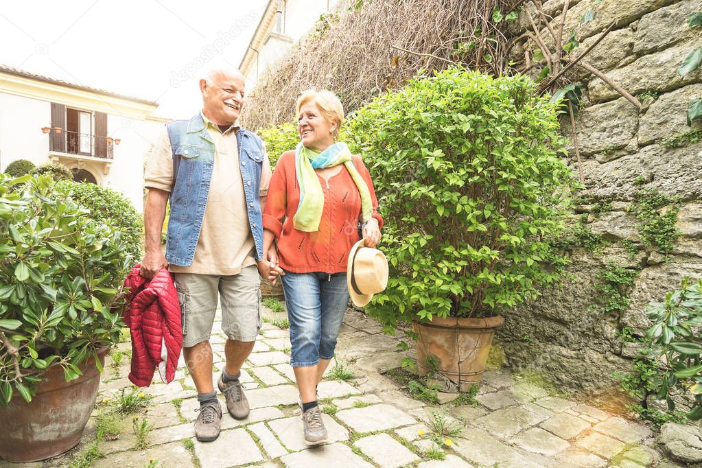 Happy senior couple walking holding hand in San Marino old town castle - Active elderly and travel lifestyle concept with retired mature people at Italy roadtrip - Sunshine halo with sunflare filter