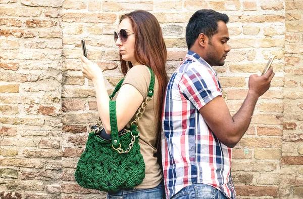 Bored multiracial couple using mobile smart phone - Addiction isolation concept with millennials young people using smartphone - Boyfriend and girlfriend on disinterest moment - Warm neutral filter — Stock Photo, Image