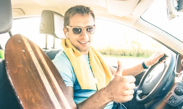 Hipster młodych moda model facet jazdy samochodów z longoboard na spring break letni nastrój - szczęśliwy człowiek pewnie z kciuk uśmiechający się, patrząc na kamery - obiektyw pochodni słońce halo z ciepły jasny filtr — Zdjęcie stockowe
