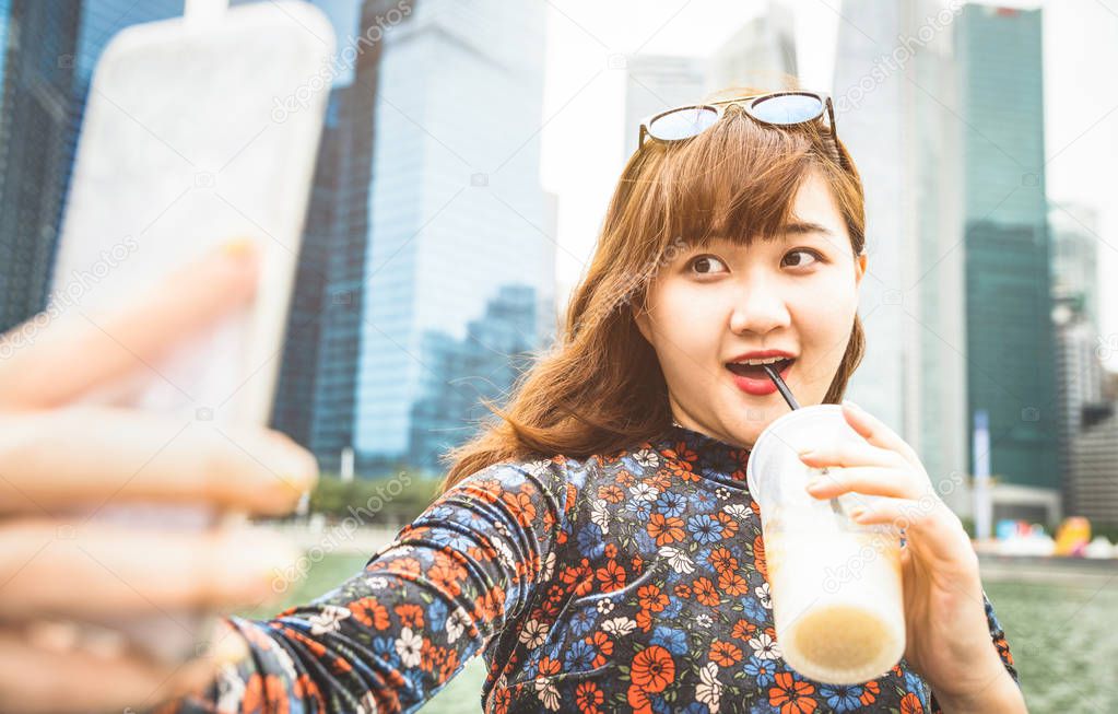 Pretty asian woman wanderer taking selfie at modern urban area of Marina Bay on Singapore skyline at sunset - Adventure travel lifestyle around south east Asia capital city - Bright warm vivid filter