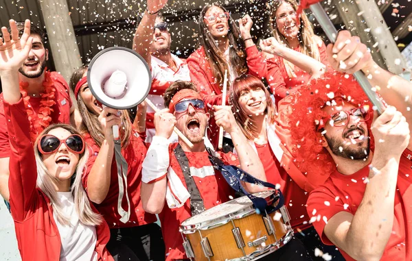 Jóvenes aficionados al fútbol animando con bandera y confeti viendo el partido de fútbol en el estadio - Amigos grupo de personas con camisetas rojas que se divierten en el concepto de campeonato mundial de deporte — Foto de Stock