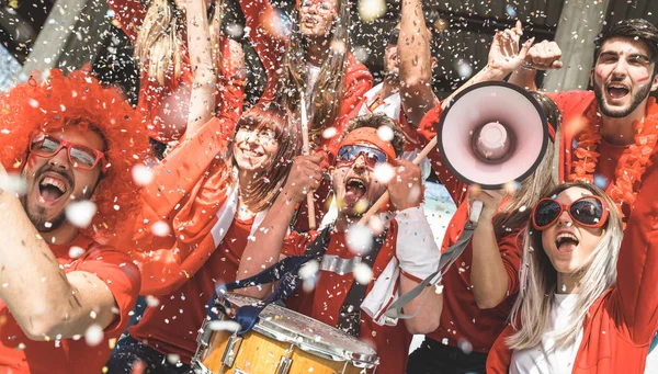 Amigos aficionados al fútbol animando con confeti viendo el evento del partido de fútbol en el estadio - Grupo de jóvenes con camisetas rojas que se divierten en el concepto de campeonato mundial de deporte — Foto de Stock