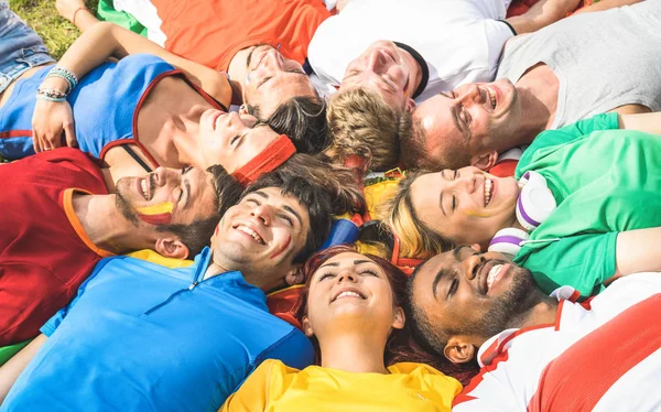 Grupo de amigos felizes deitado no prado após evento mundial de futebol - Conceito de amizade com os jovens se divertindo no festival internacional de esporte - Conceito de campeonato de Copa de futebol no filtro brilhante quente — Fotografia de Stock