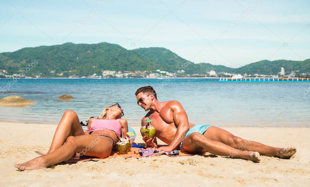 Young couple vacationer having genuine fun on tropical Phuket beach in Thailand with coconut drink - Active youth love and travel concept around world - Bright warm color filter tones