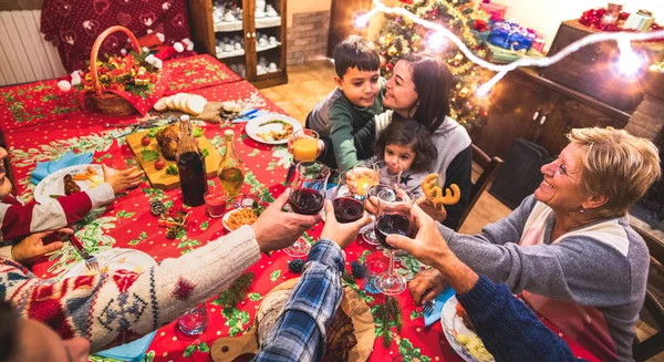 Happy multi generation family having fun at christmas supper party - New year\'s eve mood with group toasting red wine glasses - Winter holiday concept with parents and children eating together at home