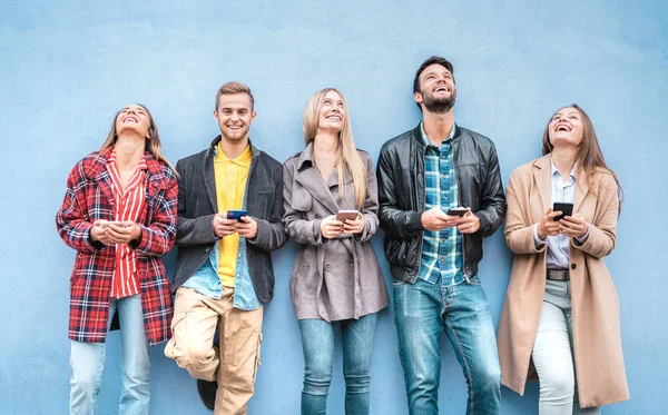 Grupo de amigos felices usando teléfonos inteligentes contra la pared azul en el receso de la universidad - Los jóvenes se divierten con el teléfono inteligente móvil - Concepto de adicción a la tecnología con millennials siempre conectados —  Fotos de Stock