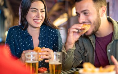 Bir çift lokanta barında hamburger yerken eğleniyor, genç mutlu insanlar kapalı yemek mekanında eğleniyor, sıcak filtreli kız yüzüne odaklanan ilişki konsepti.