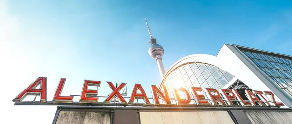 Wide angle panorama of Alexanderplatz sign at railway and subway station with tv tower behind - Side view of world famous landmark in Berlin capital of Germany - Warm vivid sunshine filter — Stock Photo, Image