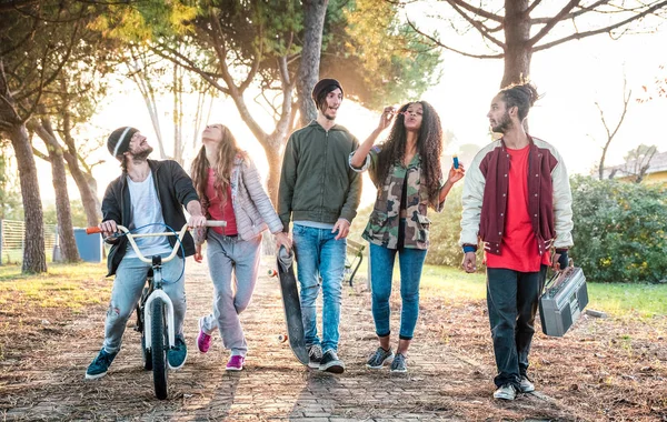 Urban friends gang walking in city skatepark on sunset backlight - Youth and millenial friendship concept with multiracial young people having fun together outdoors - Warm vivid contrast filter — Stock Photo, Image