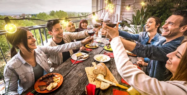 Jóvenes divirtiéndose brindando por el vino tinto juntos en la cena en la villa al aire libre - Amigos felices comiendo comida barbacoa en el patio del restaurante - Concepto de estilo de vida milenario en el filtro retro cálido - Vista amplia — Foto de Stock