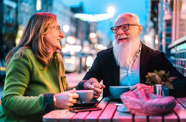 希波斯特退休的老夫妇在户外自助餐厅享受卡布奇诺-与妻子和丈夫在酒吧餐厅玩乐的快乐的老年生活理念-充满活力的霓虹灯过滤器 — 图库照片