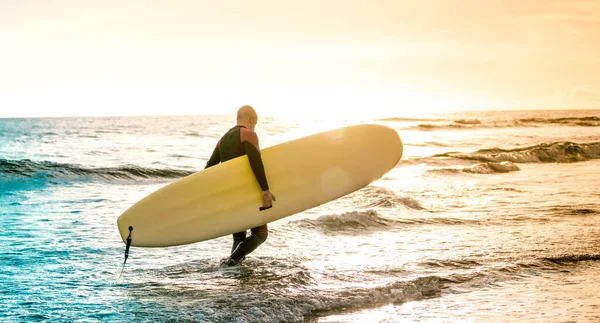 Lonely surfer walking with longboard at sunset in Tenerife - Surfing adventure lifestyle and sport travel concept - Multicolored sunshine filtered tones — Stock Photo, Image