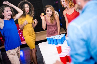 Mutlu arkadaş grubu gençlik yurdunda bira pong oynuyor - gezgin ve eğlenceli konsept gezginlerle birlikte oyun odasında gerçek bir eğlence - canlı renk filtresi ile odak kız top fırlatıyor
