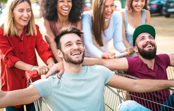 Mladí šťastní lidé, kteří se společně baví na nákupních vozících - Multiracial friends sharing funny time with trolley at commercial mall - Youth lifestyle concept with focus on middle guy - Bright filter — Stock fotografie