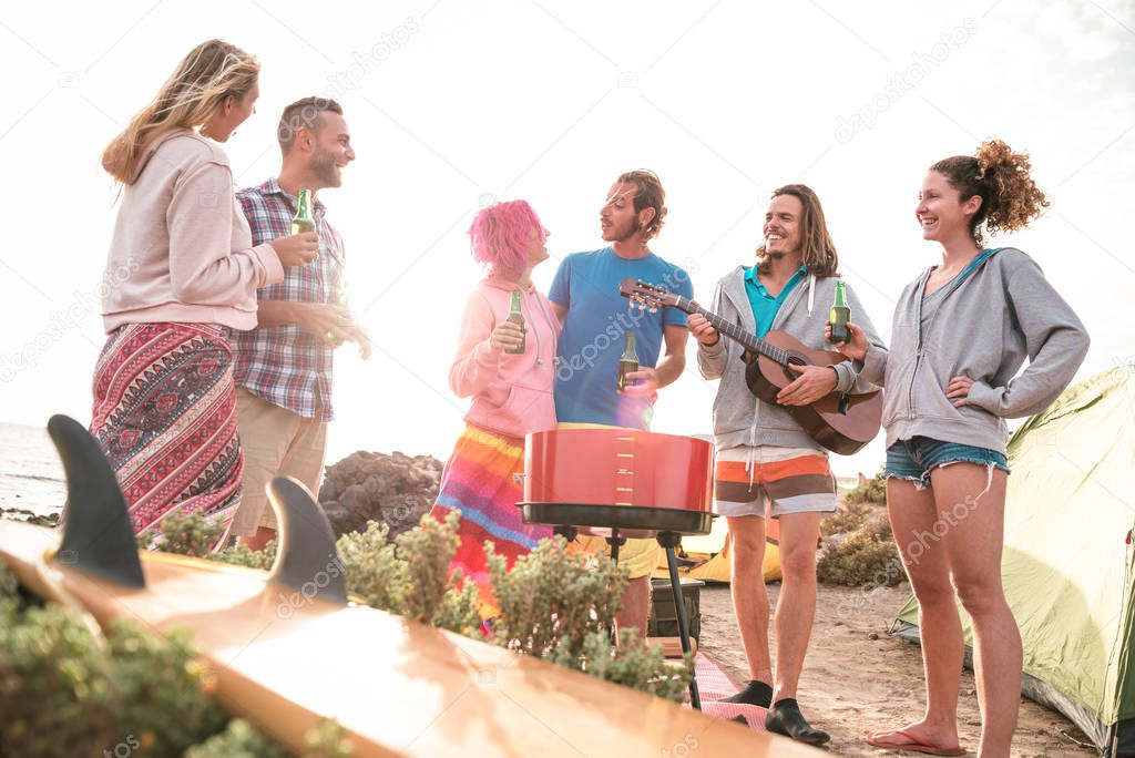Hipster friends having fun at beach camping party - Wanderlust travel concept with young people travelers toasting and drinking bottled beer together at summer surf camp - Bright sunset halo filter