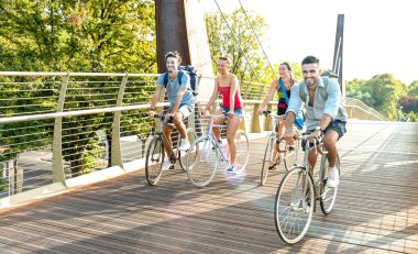 Happy millenial friends having fun riding bike at city park - Friendship concept with young millennial students biking together on bicycle lane - Bright late afternoon filter with sunshine halo