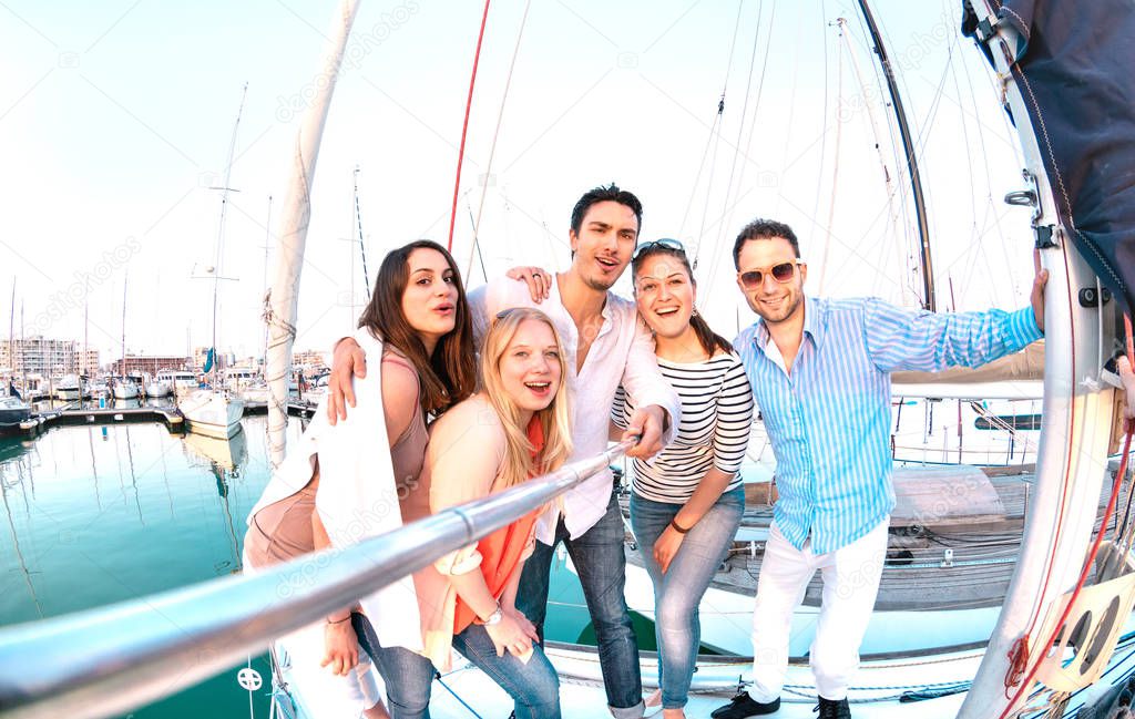 Friends group taking selfie pic with stick on luxury sailing boat party trip - Friendship concept with young millenial people having fun together at sailboat travel experience - Bright filter