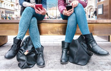 Low section of girlfriends couple sharing content on mobile smart phones - Technology addiction concept with always connected millenials - Female friends sitting in the city on social media networks