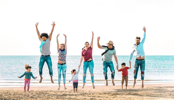 Happy multiracial families jumping together at beach holding hands - Summer vacation concept with young mixed race people having genuine fun outdoors enjoying sunset - Vivid azure backlight filter — Stockfoto