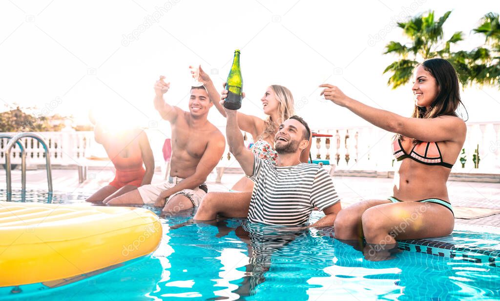 Happy friends cheering white wine champagne at swimming pool party - Luxury vacation concept with young guys and girls having fun together in summer day at hotel resort - Warm bright backlight filter